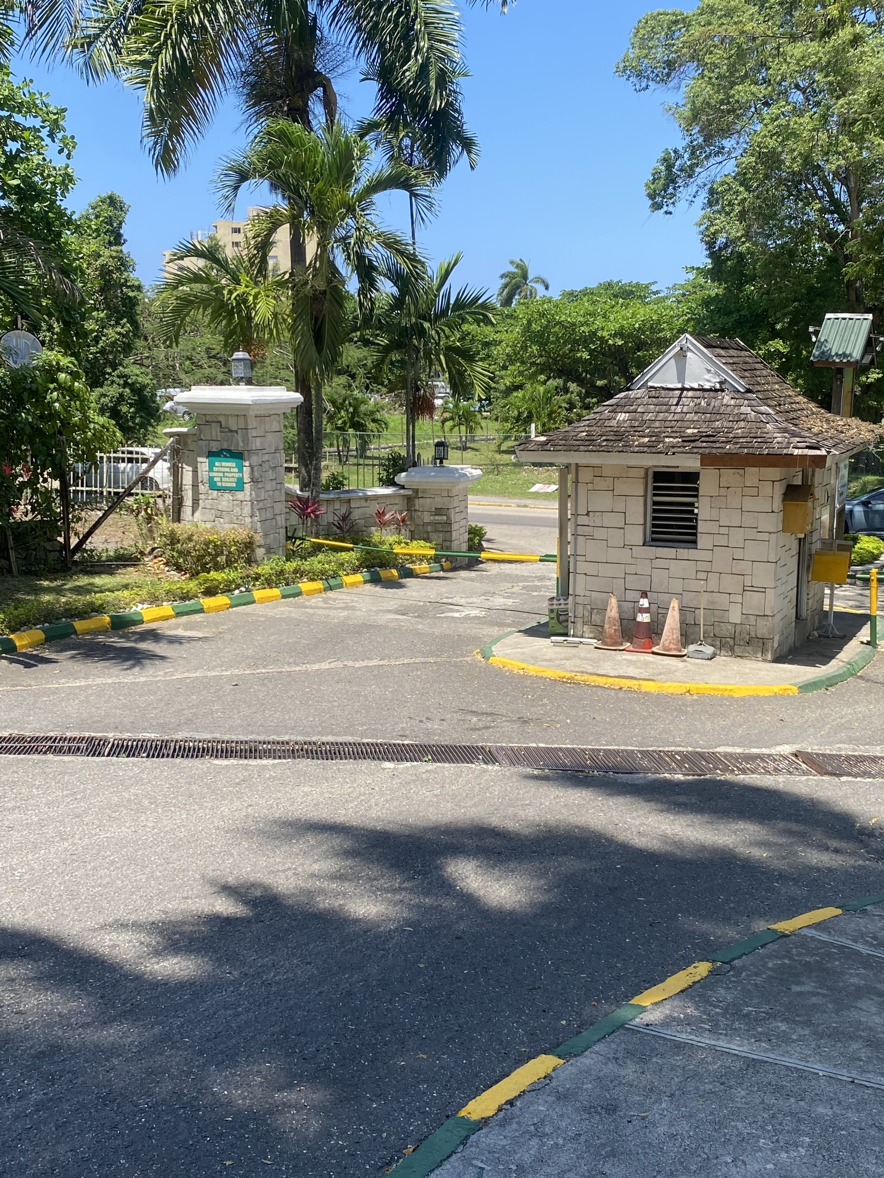 Una entrada con puerta y un pequeño edificio de piedra, palmeras y cielo despejado.