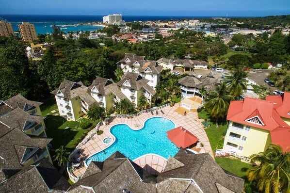 Surrounded by multiple buildings, this resort features a central swimming pool overlooking a coastal cityscape.