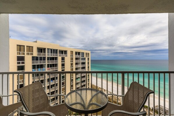 A balcony with two chairs and a small table, overlooking a beach and a hotel building. - NEWLY RENOVATED! BEAUTIFUL DESTIN BEACHFRONT CONDO WITH BREATHTAKING VIEWS! (Destin)