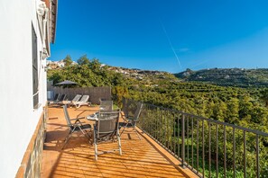 Un balcó amb sòl de fusta, barana metàl·lica i vista cap a un paisatge amb muntanyes.