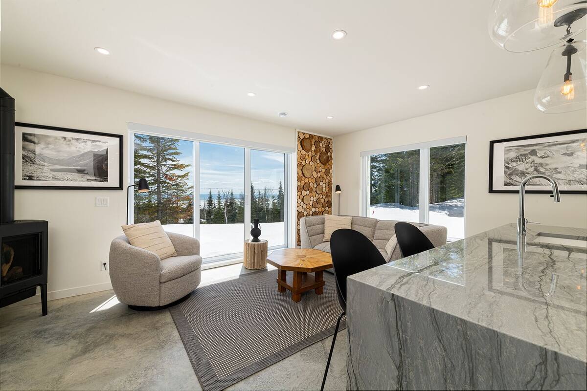 A modern kitchen with a marble countertop, a built-in stove, and a large window offering a view of a snowy landscape.