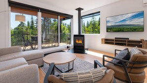 A modern living room with a fireplace, large windows, and a view of the outdoors. - Les Chalets Forêt (Petite-Riviere-Saint-Francois)