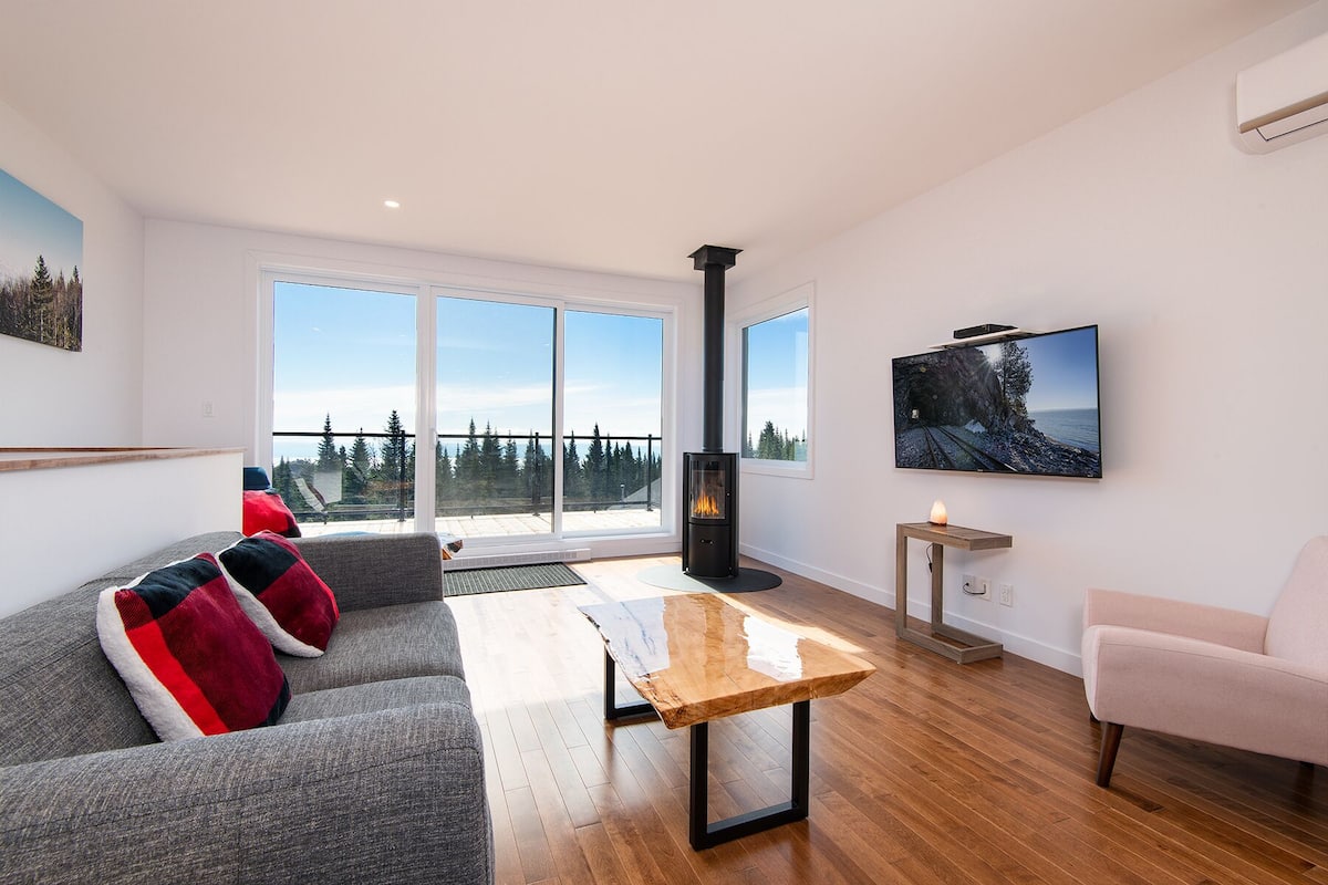 A modern living room with a sofa, a wooden coffee table, a TV mounted on the wall, and a fireplace.