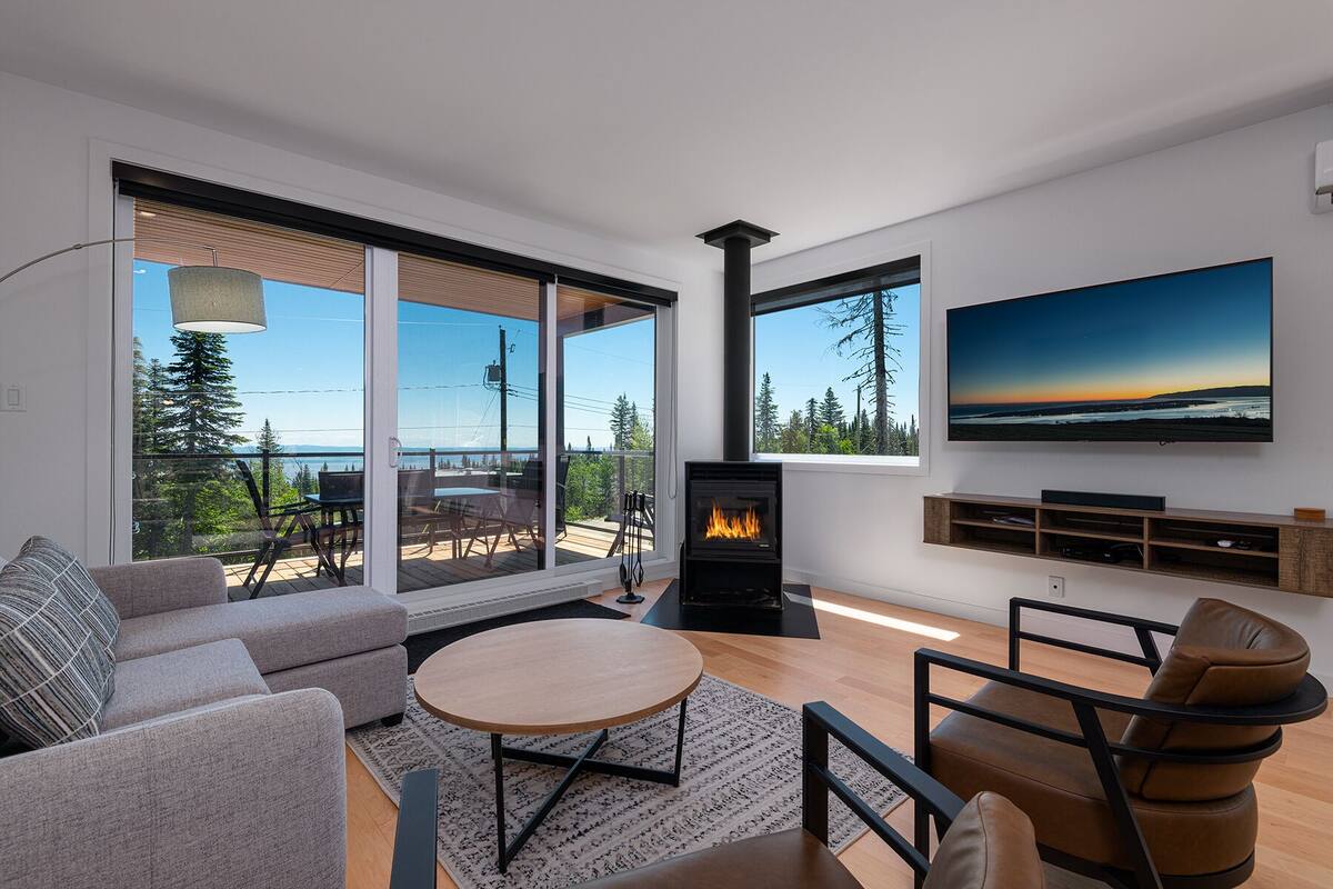 A modern living room with a fireplace, large windows, and a view of the outdoors.