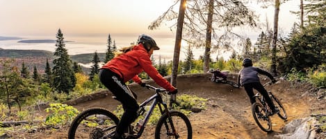 Two mountain bikers on a dirt trail with a scenic view of a forest and a body of water in the background.