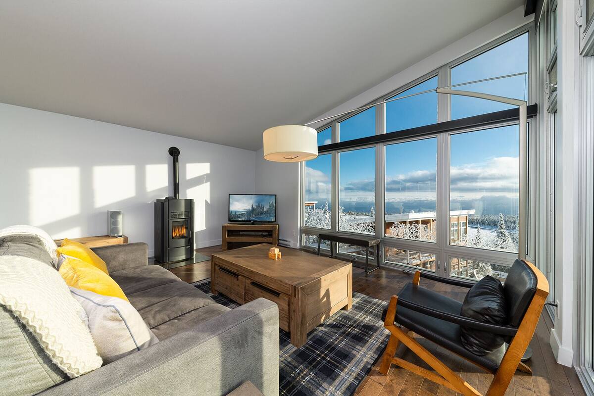 A modern living room with a large window, a fireplace, a television, and a cozy seating area.