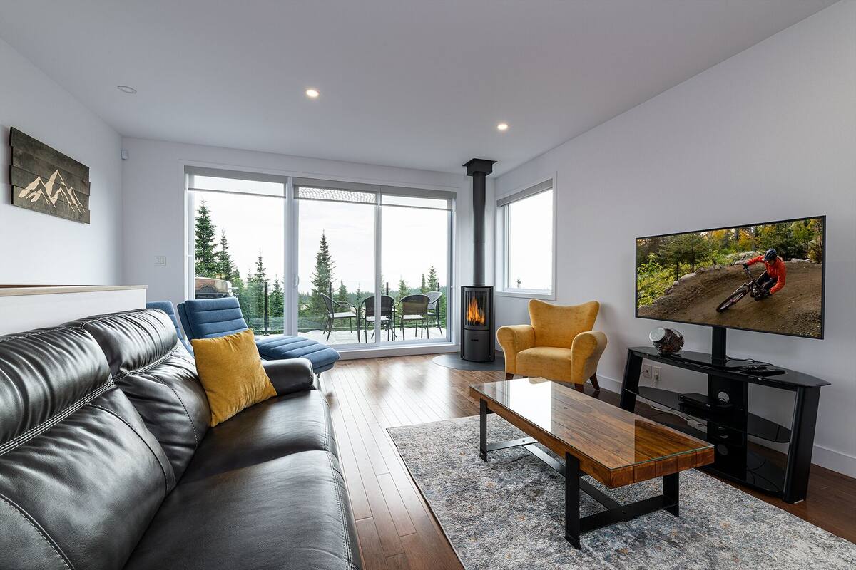 A modern living room with a leather sofa, a glass coffee table, and a television displaying a mountain biking scene.