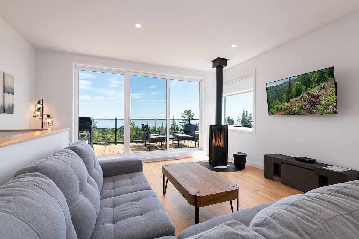 A modern living room with a large sofa, a wooden coffee table, a fireplace, and a balcony with outdoor furniture.