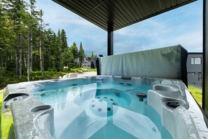 A hot tub with a covered roof, surrounded by trees and a building in the background. - Les Chalets Forêt (Petite-Riviere-Saint-Francois)
