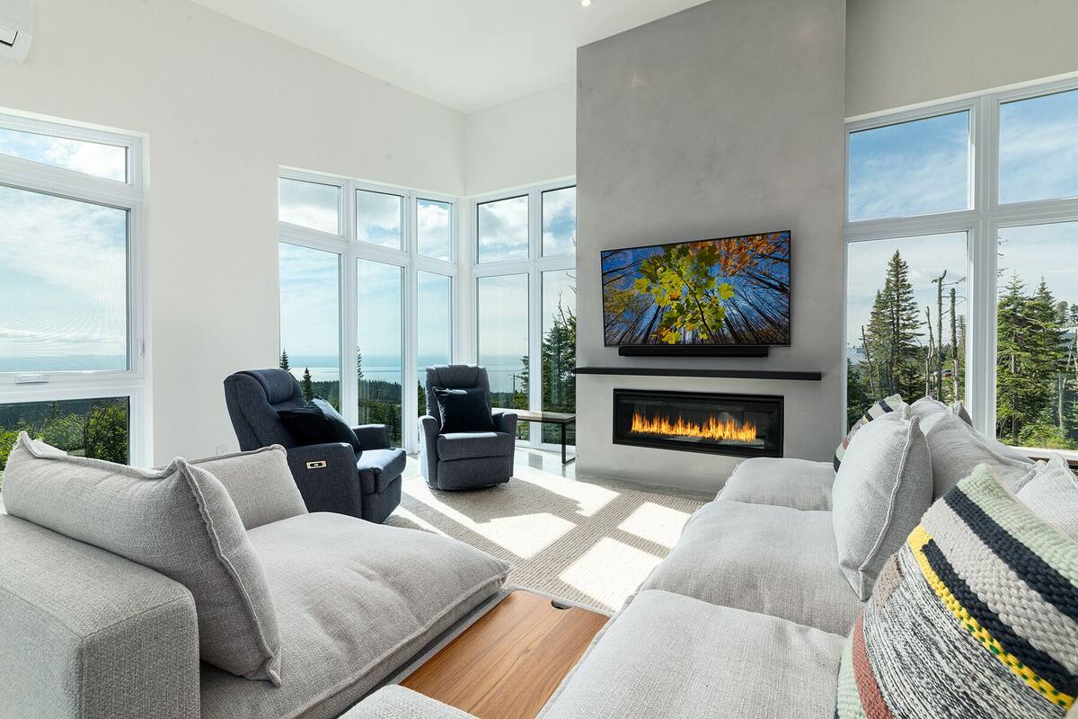 A modern living room with a fireplace, large windows, and a view of the outdoors.