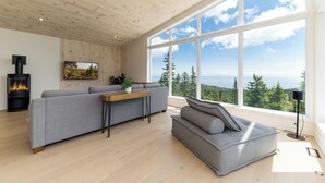 A modern living room with a large window, a fireplace, and a sofa. - Les Chalets Forêt (Petite-Riviere-Saint-Francois)