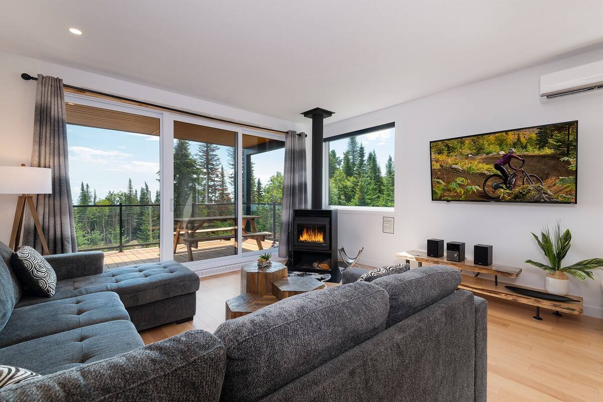 A modern living room with a fireplace, large windows, and a mountain view.