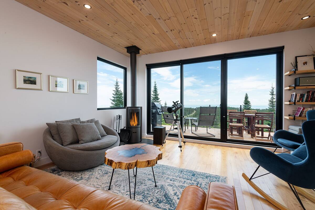 A modern living room with a fireplace, large windows, and a view of the outdoors.