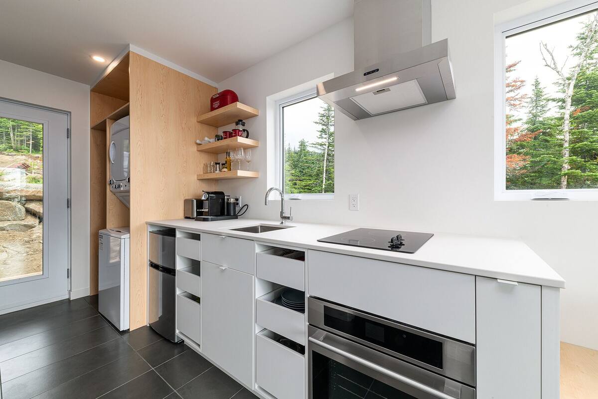 A modern kitchen with white cabinetry, a built-in oven, and a large window providing a view of trees.