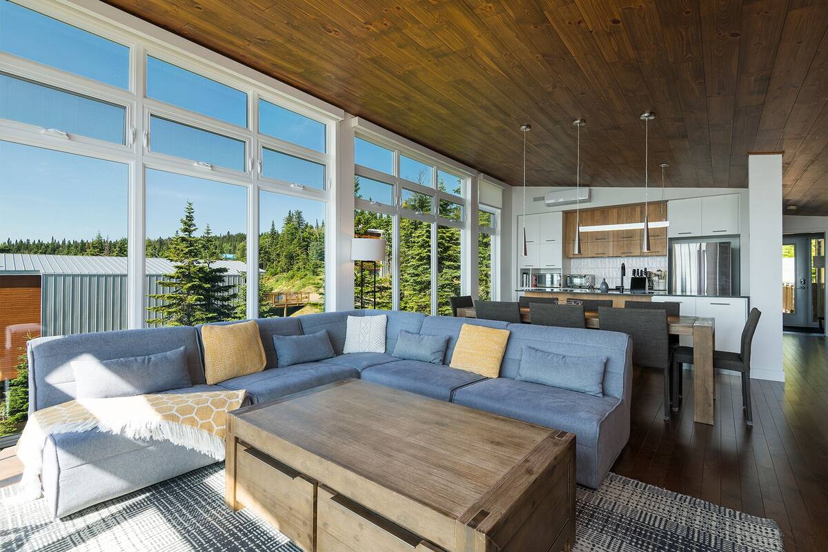 A modern living room with a large sectional sofa, a wooden coffee table, and a view of the kitchen and outdoors.