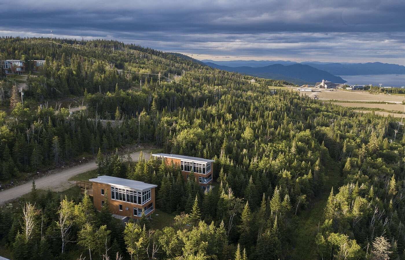A modern two-story building surrounded by dense forest, with a clear view of the surrounding landscape and distant mountains.
