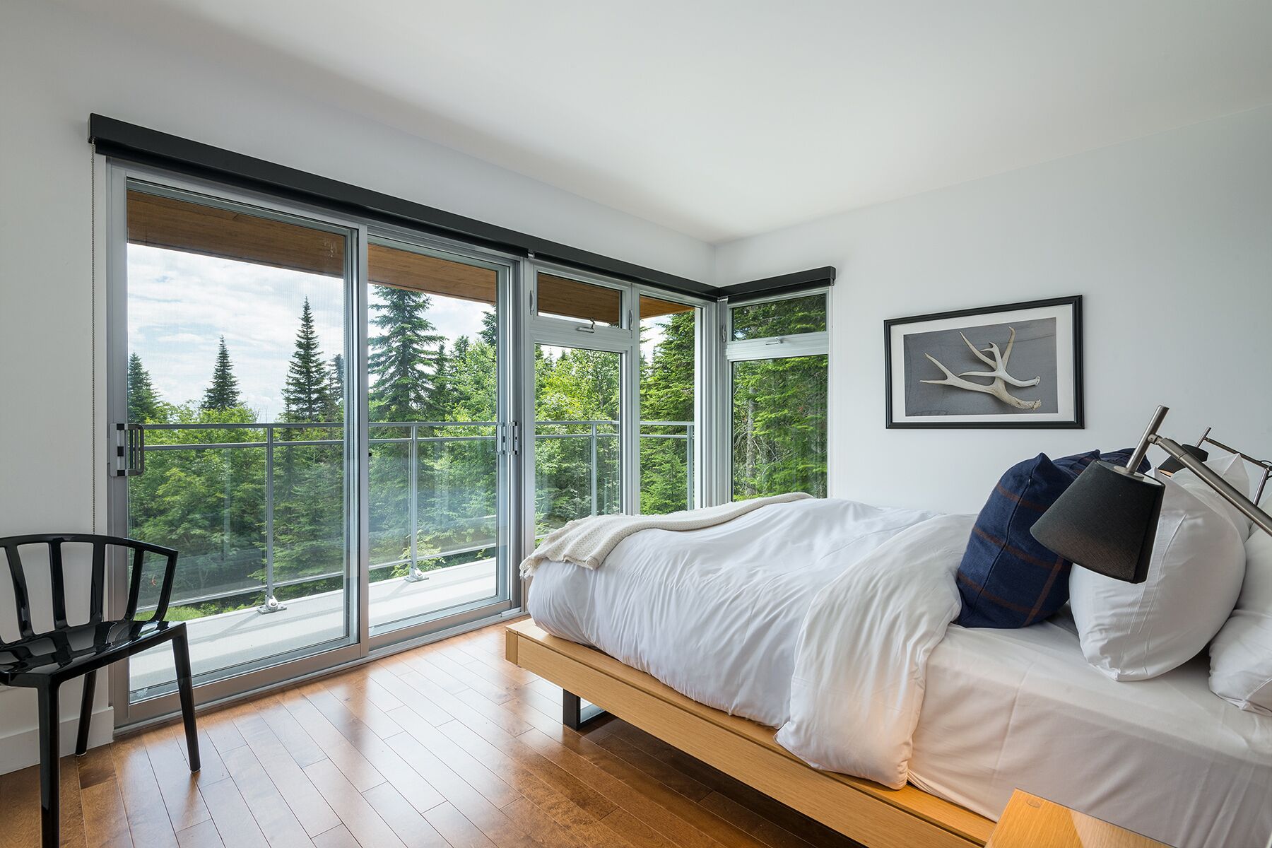 Een moderne slaapkamer met een grote schuifdeur naar een balkon, een bed met wit beddengoed en een lijst met een kunstwerk aan de muur.
