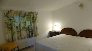 Een slaapkamer met een bed, nachtkastje, lamp, stoel en raam met gordijnen.