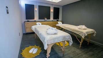 A room with two massage tables, a wooden cabinet, and a ceiling light fixture.