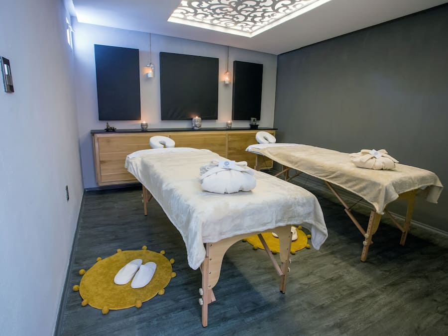 A room with two massage tables, a wooden cabinet, and a ceiling light fixture.