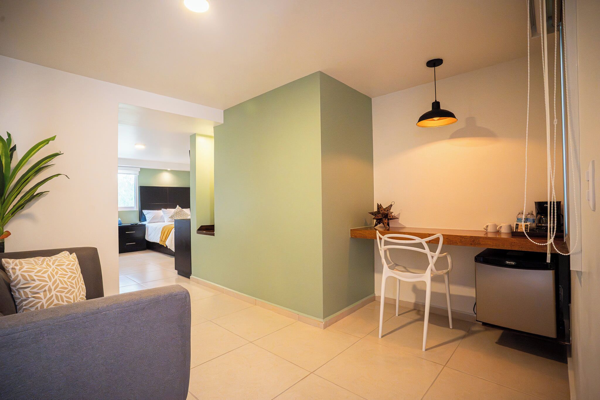 A modern living area with a sofa, a dining table with a chair, a kitchen area with a refrigerator, and a hallway leading to a bedroom.