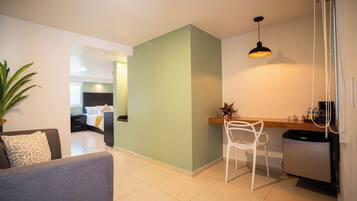A modern living area with a sofa, a dining table with a chair, a kitchen area with a refrigerator, and a hallway leading to a bedroom.