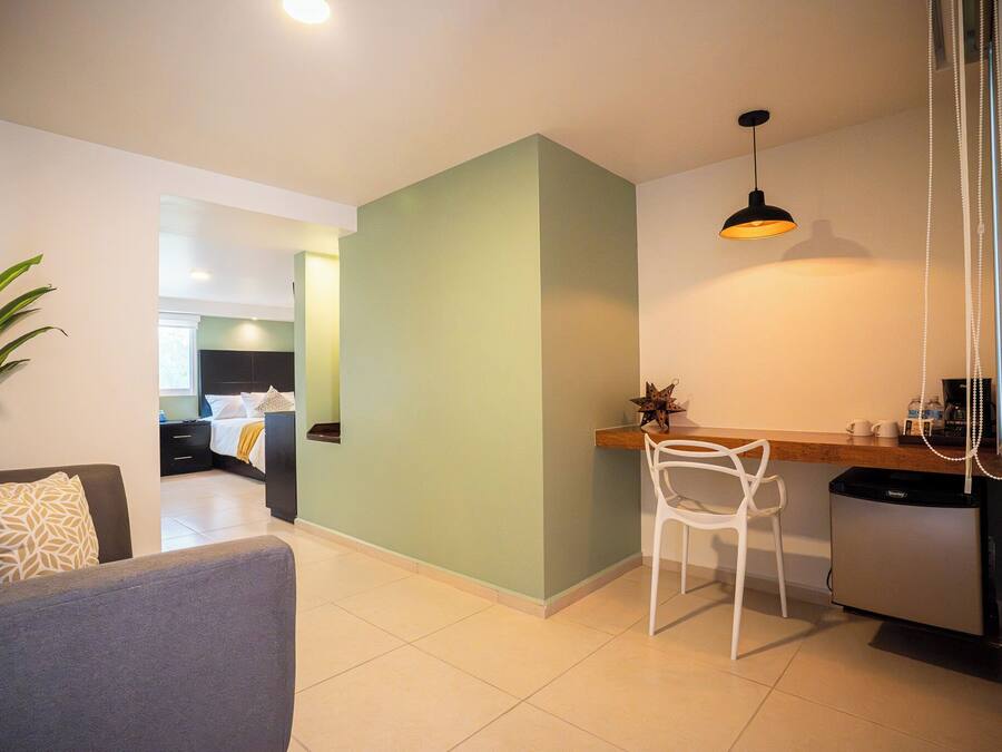 A modern living area with a sofa, a dining table with a chair, a kitchen area with a refrigerator, and a hallway leading to a bedroom.