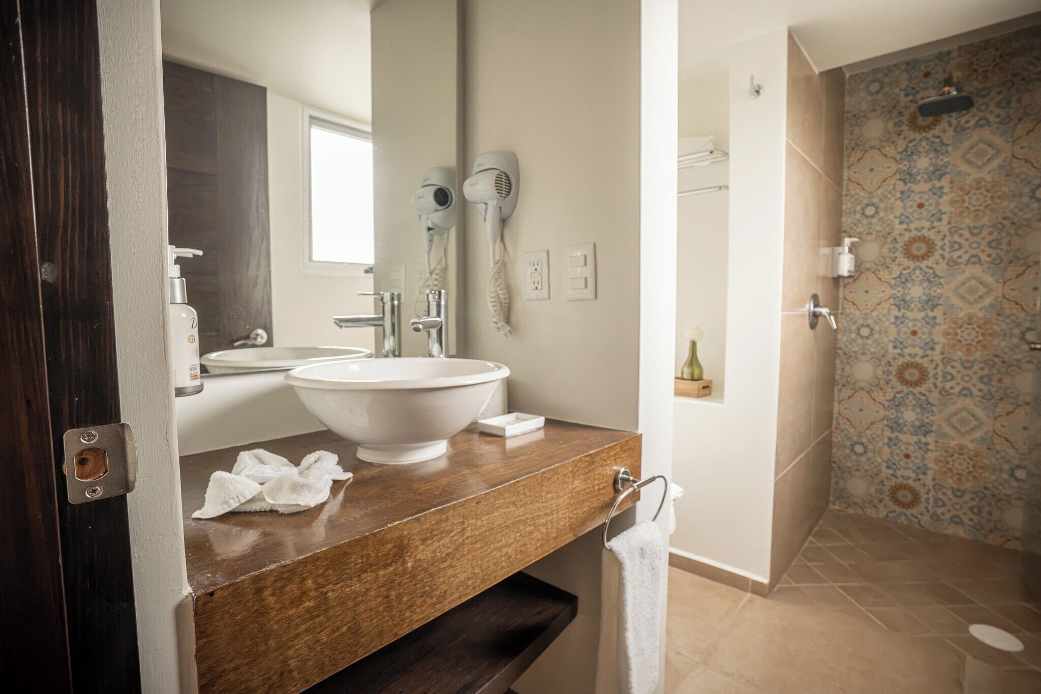 A bathroom with a large sink, a mirror, a hairdryer, and a shower with patterned tiles.