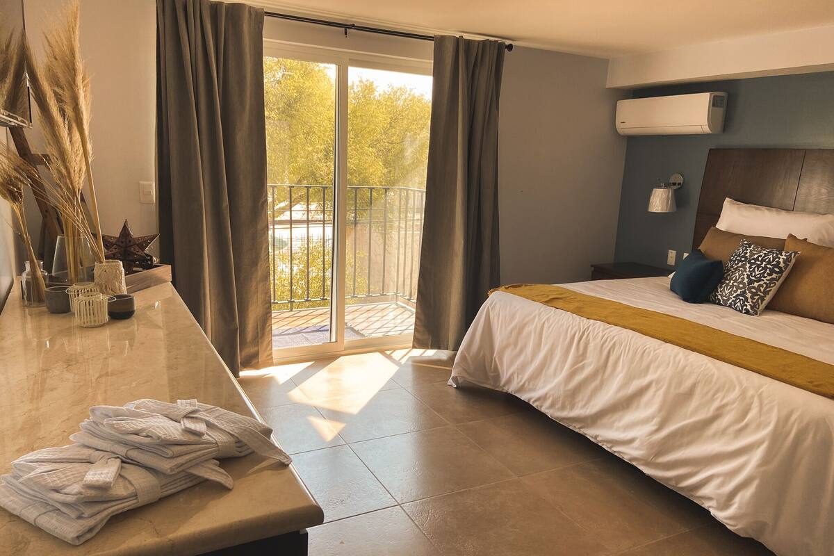 A hotel room with a bed, a bathroom area, and a balcony with curtains.