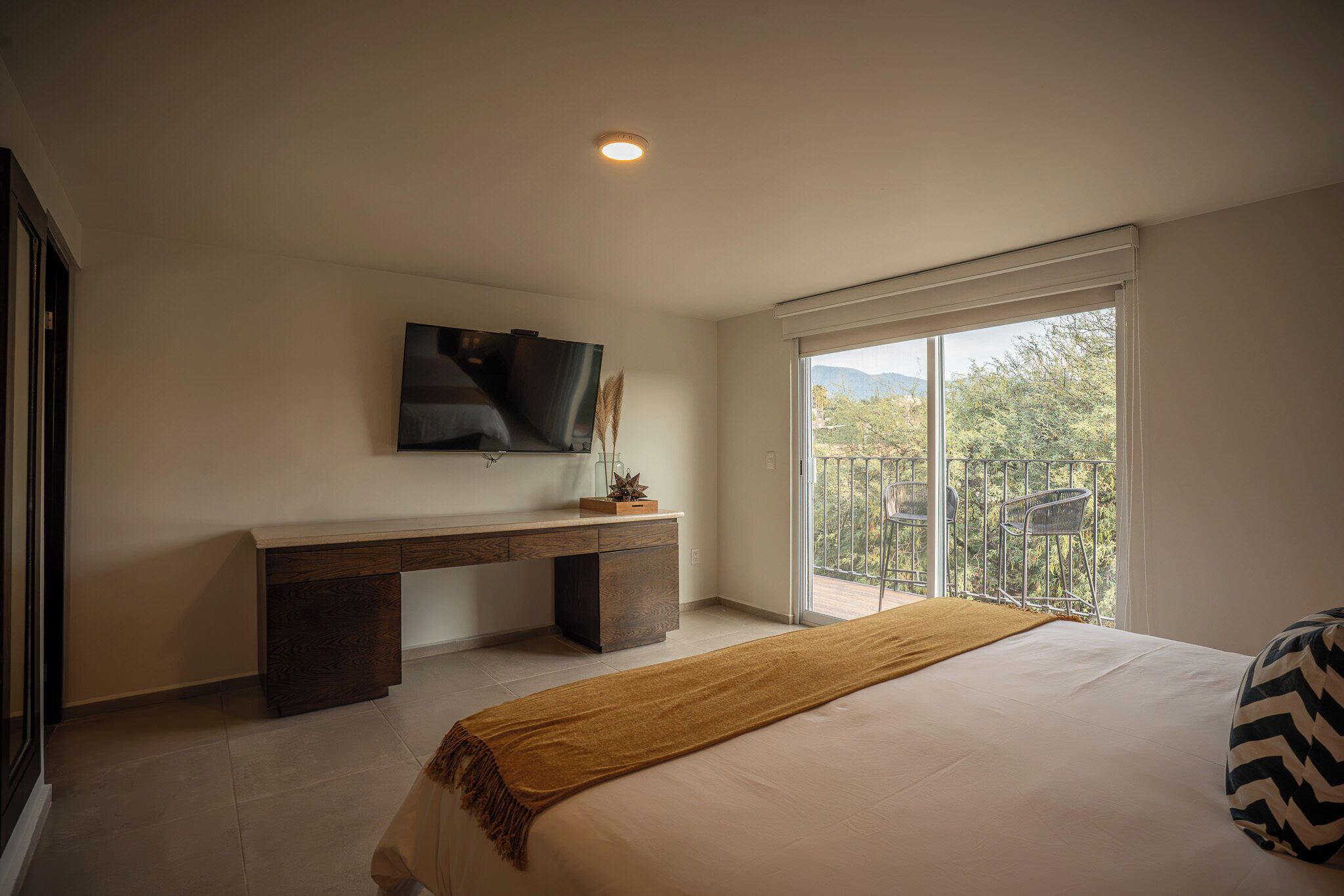 A bedroom with a bed, a desk, a TV, and a balcony with a view.