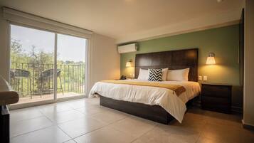 A bedroom with a large bed, two bedside lamps, a nightstand, a sliding glass door to a balcony, and an air conditioning unit.