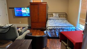 Een slaapkamer met een bed, een houten kledingkast, een televisie aan de muur en een raam met jaloezieën.