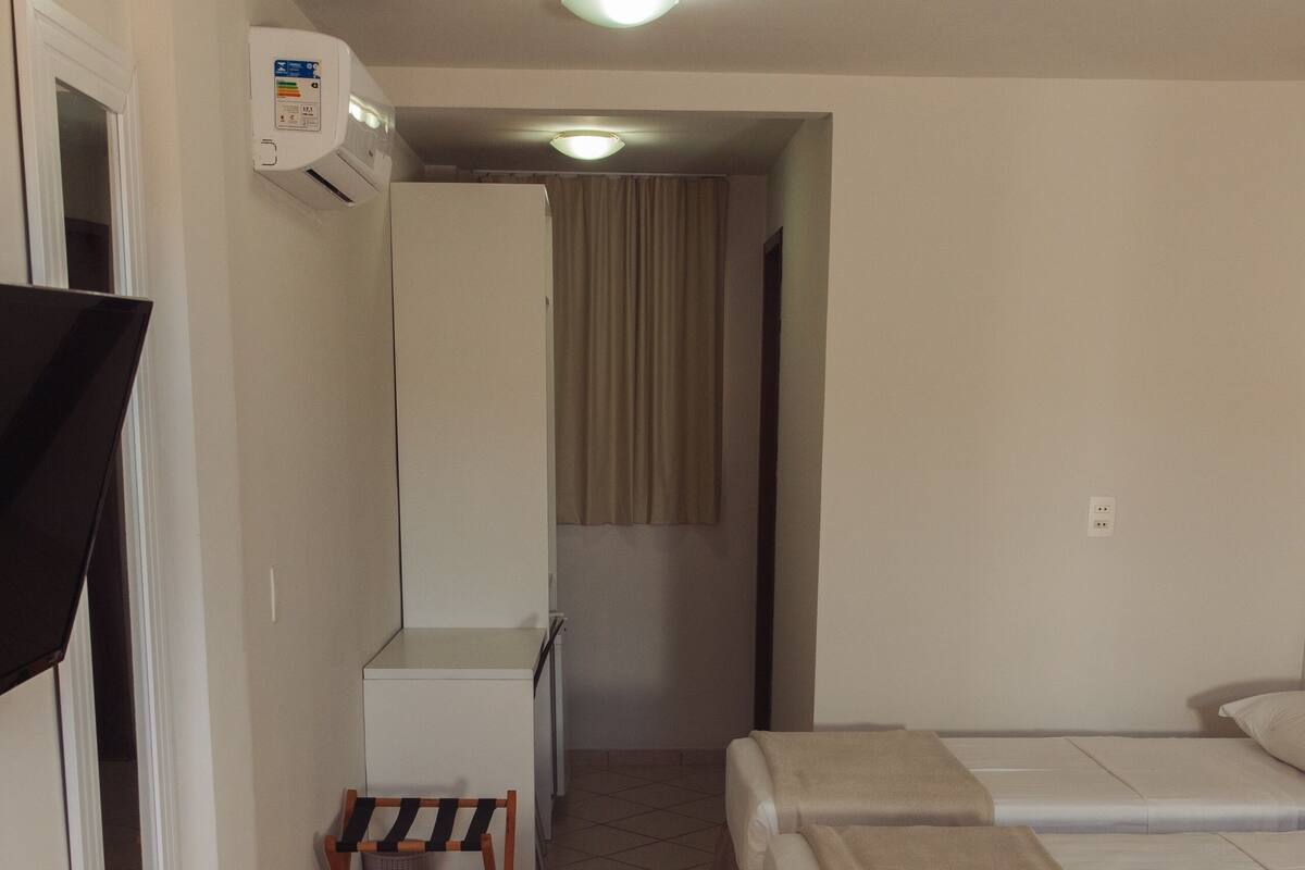 A hotel room with two beds, a small table, a chair, and an air conditioning unit.