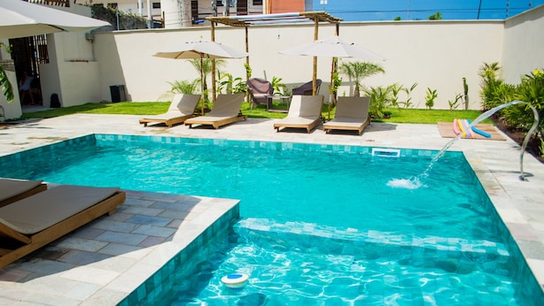 A swimming pool with lounge chairs and umbrellas, surrounded by a tiled patio and greenery. - Pousada Laranja Durigon  (Natal)