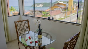 A glass table with a bottle of wine and glasses, two wicker chairs, and a view of a coastal area through large windows. - Pousada Laranja Durigon  (Natal)