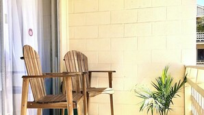 A balcony with two wooden chairs, a small potted plant, and a striped rug. - The Bungalow, 2nd row from Ocean, Pool/Hot Tub! (Myrtle Beach)
