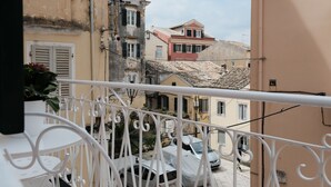 A balcony with a white metal railing overlooking a narrow street with buildings.