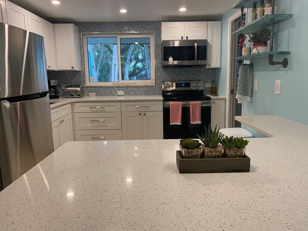 A modern kitchen with stainless steel appliances, a large island, and a window with a view of trees.