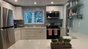 A modern kitchen with stainless steel appliances, a large island, and a window with a view of trees. - Beautiful Home,ON THE KEY🏝️ FreeBikes,BeachChairs,FirePit,Kayaks,Newly Renovated  (Englewood)
