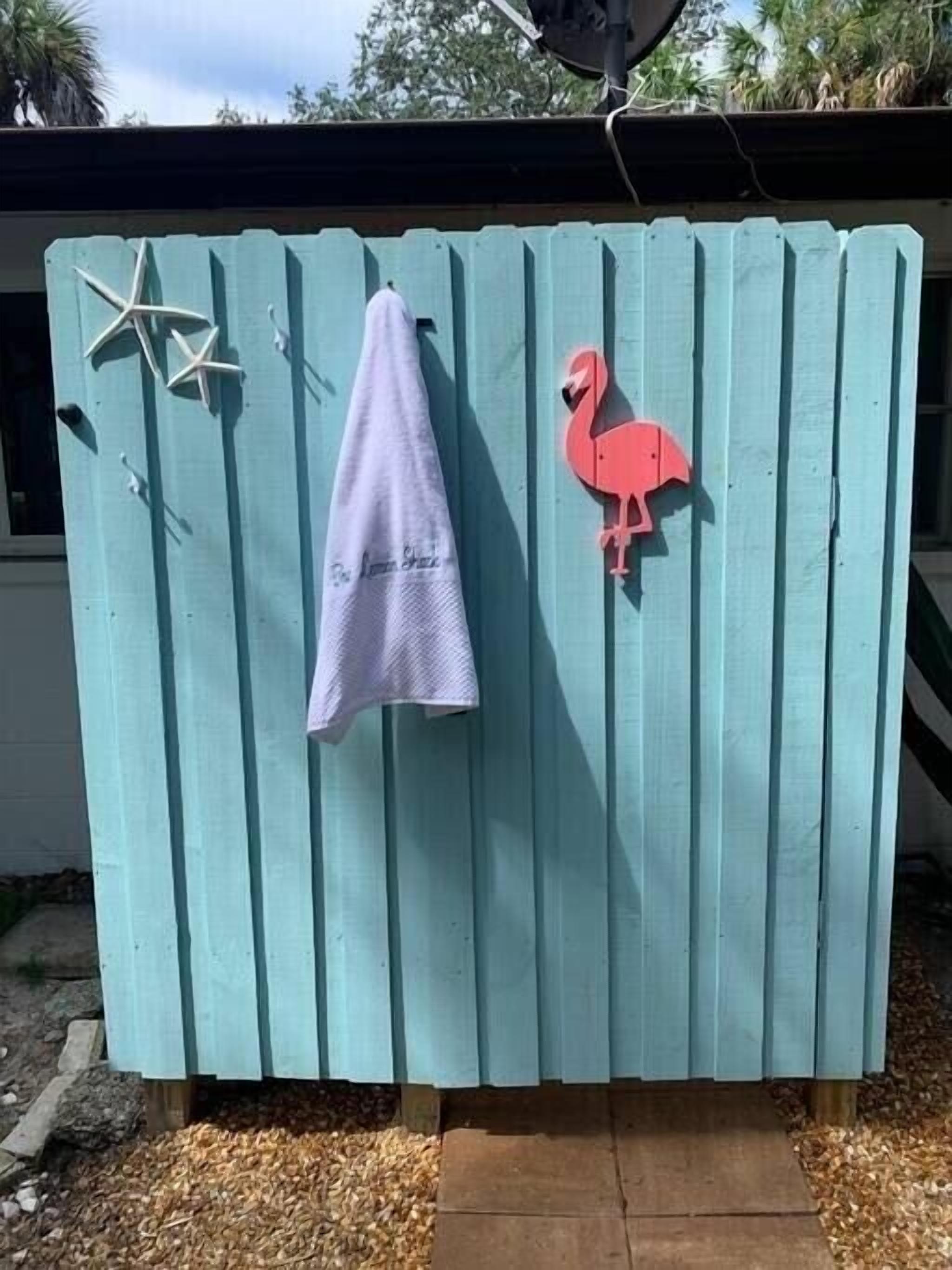 Ein türkisfarbener Holzzaun, an dem ein Handtuch hängt und eine rosa Flamingo-Dekoration angebracht ist.