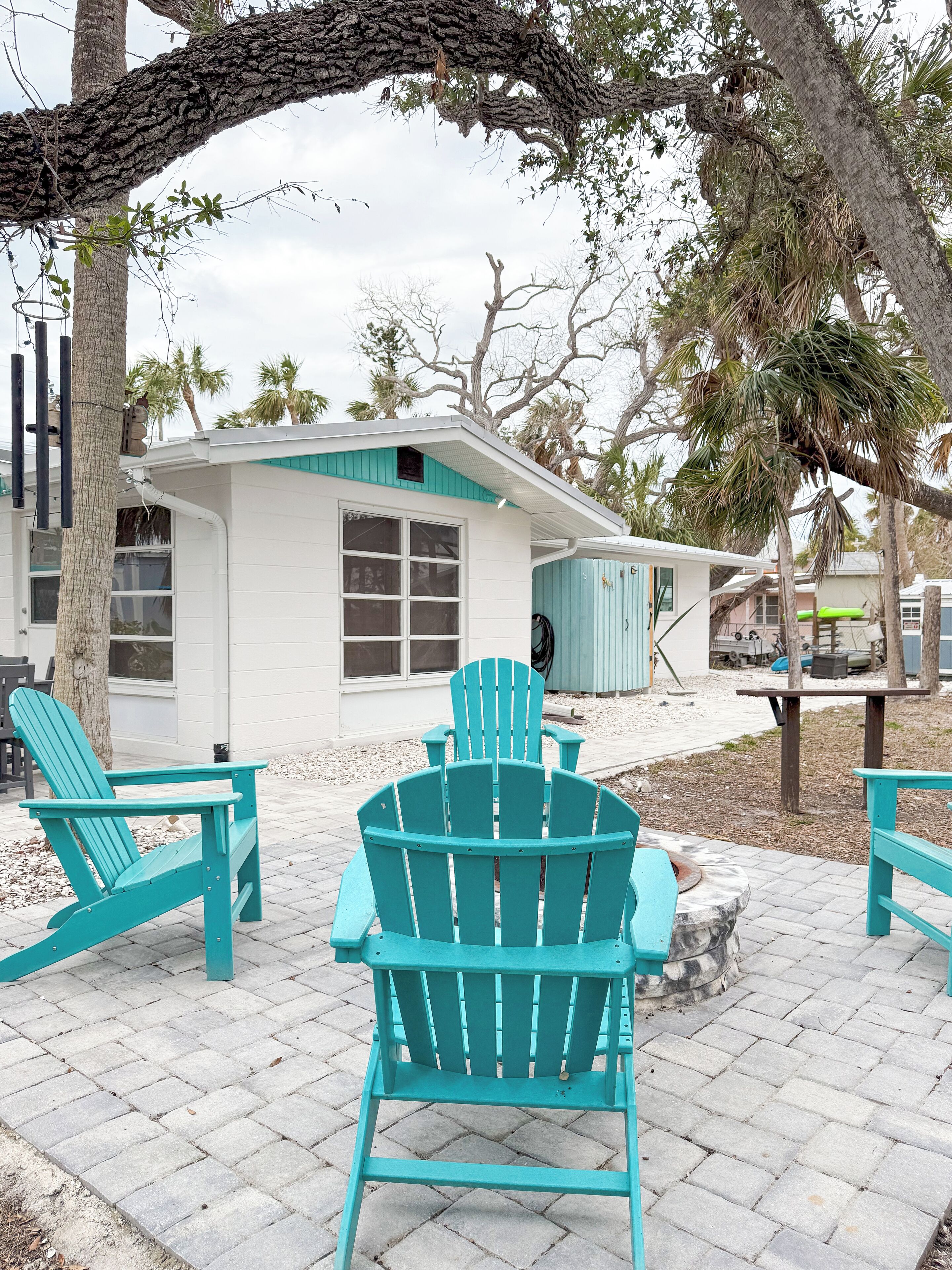 Een huis met een witte gevel en een blauwe deur. Twee turkozen Adirondack-stoelen en een klein tafeltje staan ervoor.