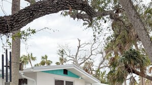 A house with a white exterior and a blue door. There are two turquoise Adirondack chairs and a small table in front of the house. - Beautiful Home,ON THE KEY🏝️ FreeBikes,BeachChairs,FirePit,Kayaks,Newly Renovated  (Englewood)