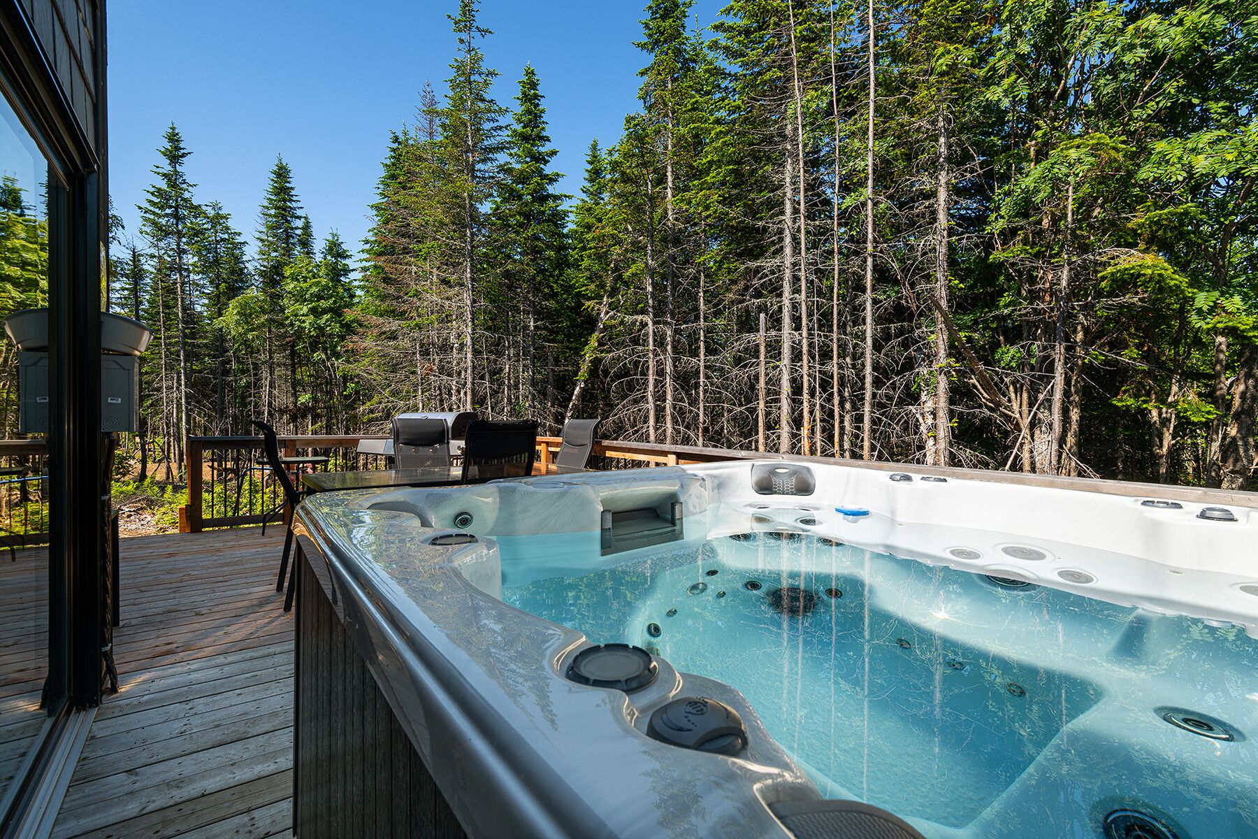 A hot tub with a wooden deck and a view of a forest.