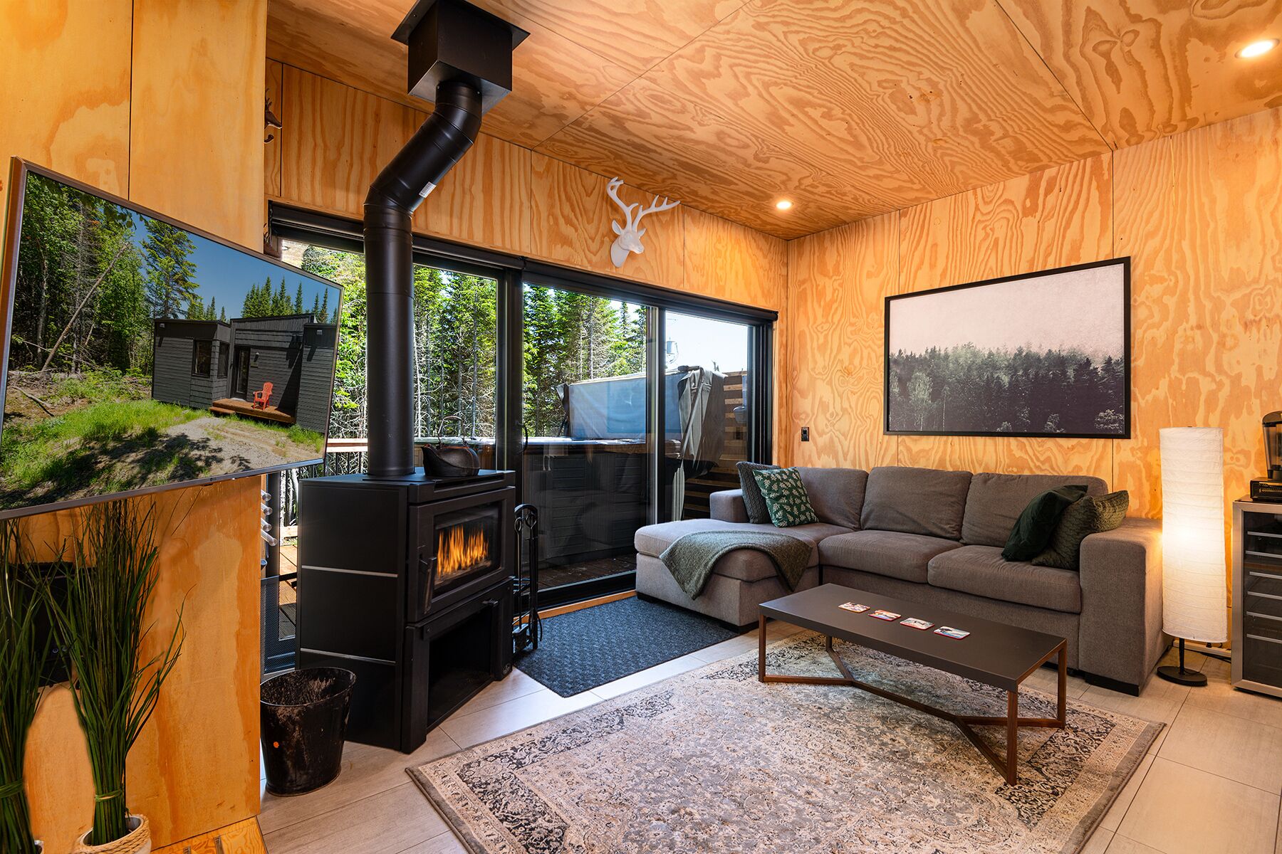 Un salon chaleureux avec un poêle à bois, une grande fenêtre et un tableau représentant un paysage, encadré.