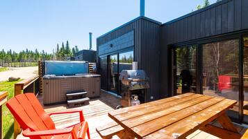 Une terrasse extérieure avec une table et des chaises en bois, un jacuzzi et un barbecue.