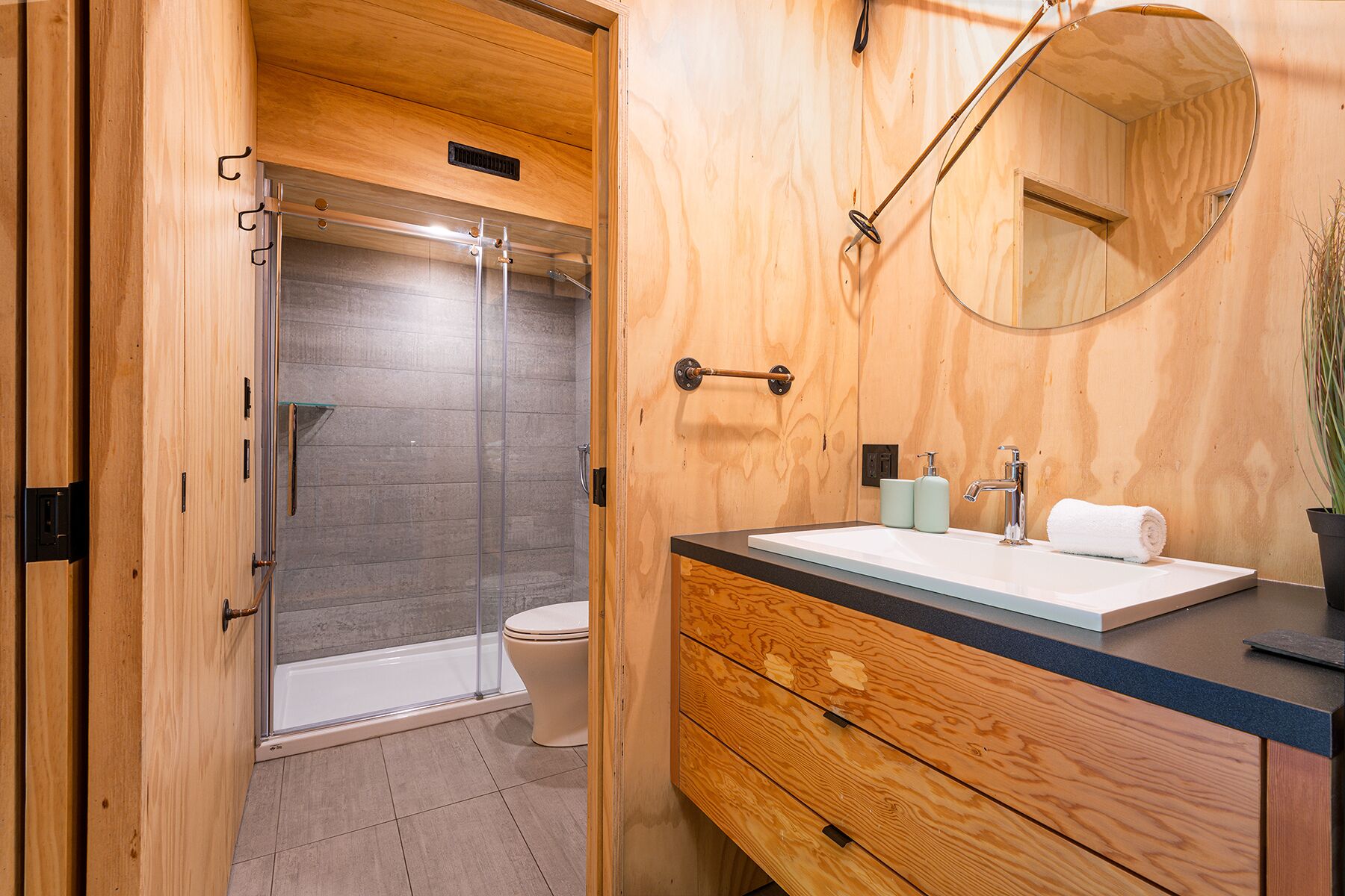 A modern bathroom with a glass-enclosed shower, a toilet, a wooden vanity with a sink, and a mirror.