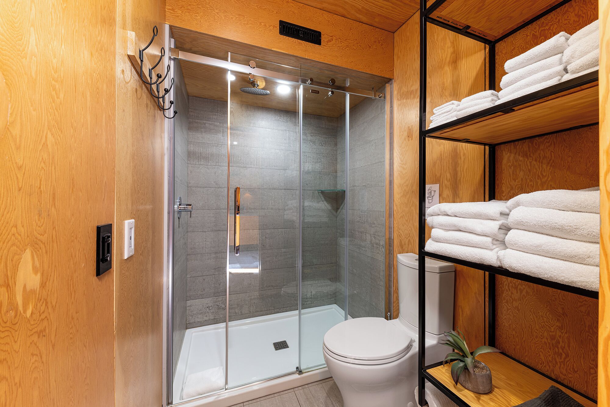 A modern bathroom with a glass-enclosed shower, a toilet, and shelves with neatly folded towels.