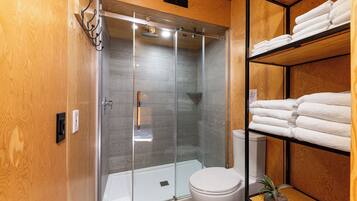 A modern bathroom with a glass-enclosed shower, a toilet, and shelves with neatly folded towels.