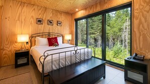 A bedroom with a large window, a bed, a bench, and a desk with a phone. - Les Refuges (Petite-Riviere-Saint-Francois)