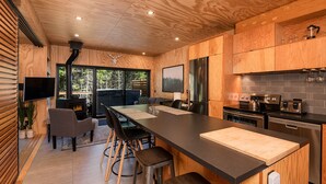 A modern kitchen with wooden cabinetry, a large island, and a dining area with a fireplace. - Les Refuges (Petite-Riviere-Saint-Francois)